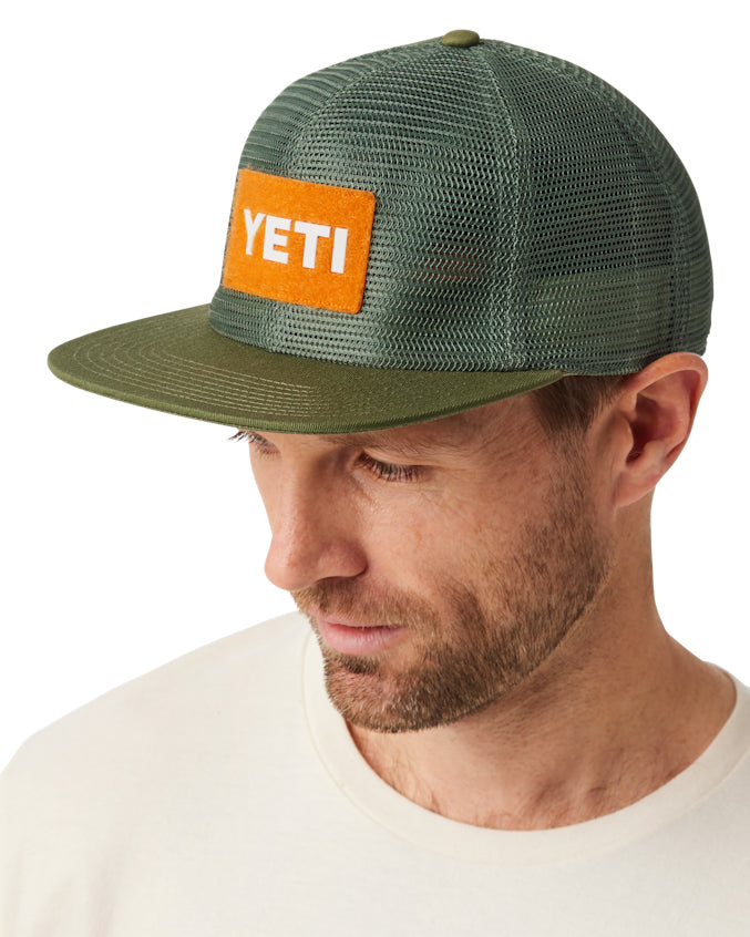 Man wearing an olive green YETI cap with a bright orange patch displaying the YETI logo, styled with a breathable mesh design.